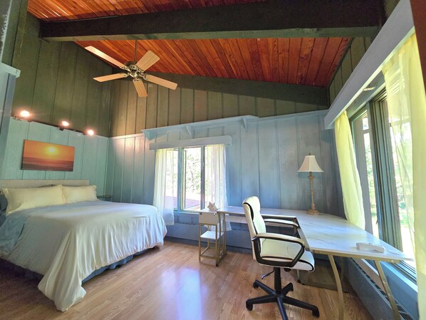 Un dormitorio con cama, escritorio, silla, ventilador de techo y ventana con cortinas.