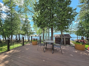 Une terrasse en bois avec une table et des chaises, entourĂ©e dâarbres et donnant sur une Ă©tendue dâeau.