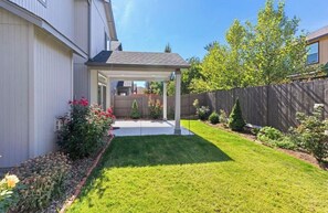 Ein Garten mit überdachter Terrasse, Holzzaun und verschiedenen Pflanzen.