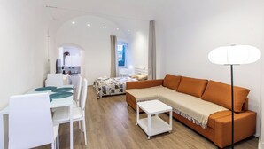 A modern, well-lit room with a sofa, dining table, and chairs, a small white table, and a lamp. - Palma Cabin Renovated Apartment Old Town, Sanremo, Italy (Sanremo)