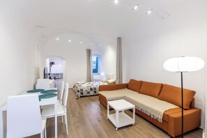 Ein moderner, gut beleuchteter Raum mit einer Couch, einem Esstisch mit Stühlen, einem kleinen weißen Tisch und einer Lampe.