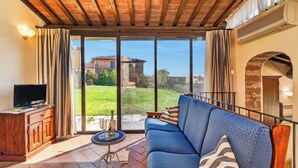 Una habitación con techo de madera, un sofá, un televisor y vistas a un jardín y un edificio.