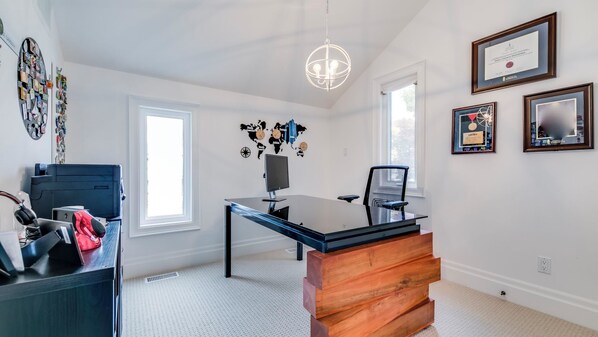 A modern office space with a glass desk, a black office chair, a wooden sideboard, a globe wall decoration, and framed certificates on the wall.