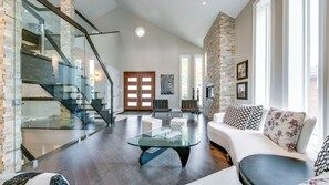 A spacious living area with a glass coffee table, a white sofa, and a staircase with glass railings.