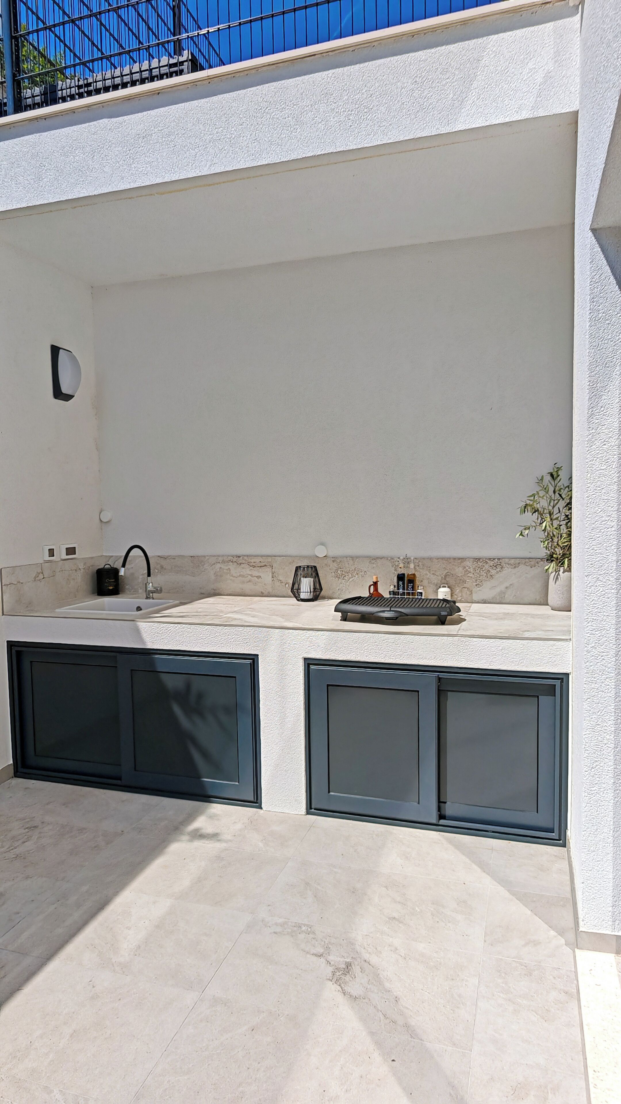 An outdoor kitchen area with a sink, a kettle, and a small plant.