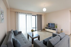 Ein modernes Wohnzimmer mit grauem Sofa, einem Couchtisch, einem Fernseher auf einem Schrank und einer Schiebetür aus Glas.