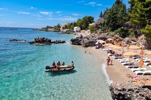 A beach with clear turquoise water, rocky outcrops, and a row of sun loungers with umbrellas. - Velaris Sea View Balcony 201, Vlore, Albania (Vlore)