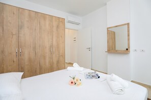 Ein Hotelzimmer mit großem Holzschrank, einem Bett mit weißer Bettwäsche, einem Spiegel und einem kleinen Tisch mit Zeitschrift und Handtüchern.