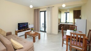 Ein Wohnzimmer mit einer Couch, einem Fernseher, einem Couchtisch und einem Essbereich mit Stühlen und einem Tisch.