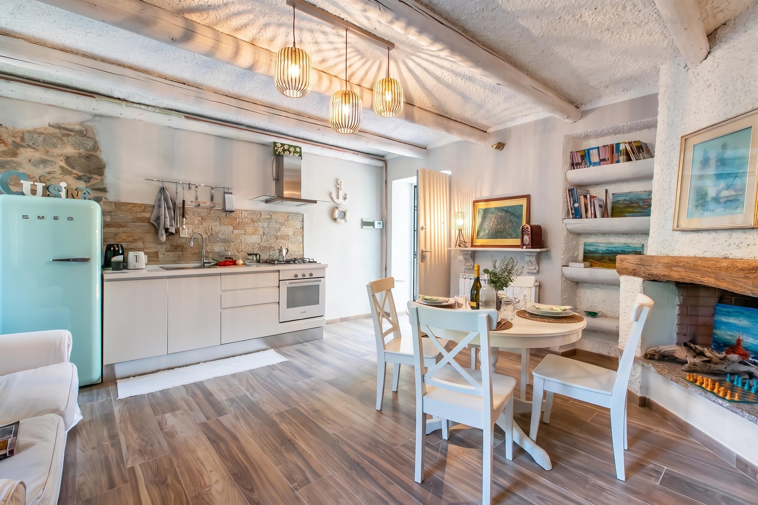 Eine moderne Küche mit weißen Schränken, einer Wand mit Steinverkleidung und einem Essbereich mit weißen Stühlen und einem runden Tisch.