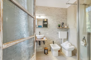 Un baño moderno con lavamanos sobre encimera, bidé e inodoro, que presenta una pared de piedra y detalles de madera.