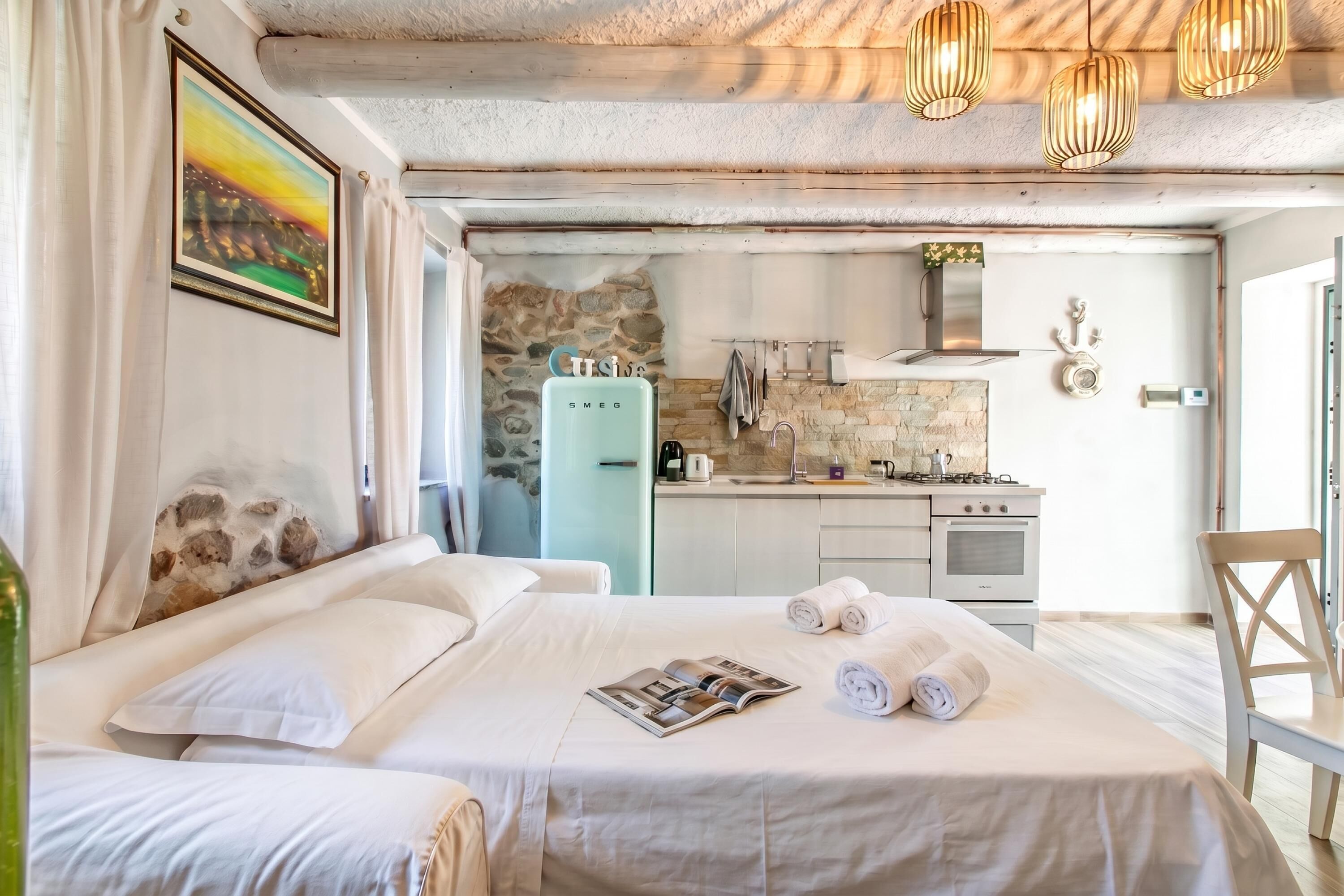 Ein Hotelzimmer mit einem Bett, einer Zeitschrift, Handtüchern, einer Küchenzeile mit Herd und einer Steinwand.