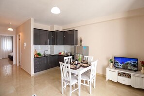 A modern kitchen with dark cabinets, a dining table with white chairs, and a flat-screen TV on a white cabinet. - Velaris Sea View Balcony 104, Vlore, Albania (Vlore)