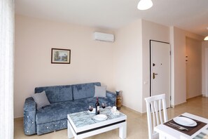 A living room with a blue sofa, a dining table set with plates, wine glasses, and a bottle, and a door in the background. - Velaris Sea View Balcony 104, Vlore, Albania (Vlore)