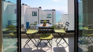 A balcony with a table and chairs, a potted plant, and a view of the sea and buildings. - Velaris Sea View Balcony 103, Vlore, Albania (Vlore)
