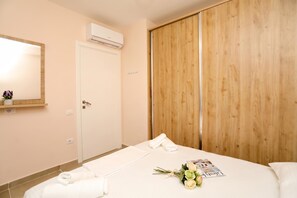 A hotel room with a bed, a wooden wardrobe, a wall-mounted air conditioner, and a bedside table with a magazine and flowers. - Velaris Sea View Balcony 103, Vlore, Albania (Vlore)