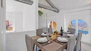 Un comedor con una mesa dispuesta para cuatro personas, vista al mar y un balcón con barandilla.