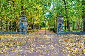 Una entrada a un parque con pilares de piedra, un camino pavimentado y árboles.
