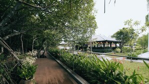 A pathway lined with greenery, a covered seating area, and a view of a building in the distance. - Madu River Reach (Balapitiya)
