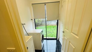 A laundry room with a washing machine, a drying rack, and a door leading to a covered outdoor area. - Peaceful corner retreat|Park Side | 3 Bed, 2 Bath (Cranbourne West)