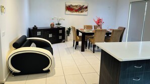 A modern dining area with a black and white sofa, a dining table set for four, and a large abstract painting on the wall. - Peaceful corner retreat|Park Side | 3 Bed, 2 Bath (Cranbourne West)