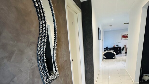 A hallway with a decorative mirror, a glass table with flowers, and a view into a dining area. - Peaceful corner retreat|Park Side | 3 Bed, 2 Bath (Cranbourne West)