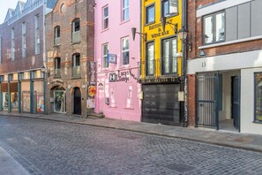 Una calle con edificios, incluyendo un edificio rosa con un letrero que dice 'Lucy Lounge' y un edificio amarillo con un letrero que dice 'Restaurante & Wine Bar'.