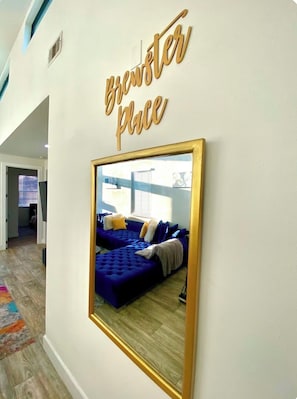 Ein Zimmer mit einem großen Spiegel, der ein blaues Sofa und ein Schild mit der Aufschrift 'Brewster place' reflektiert.