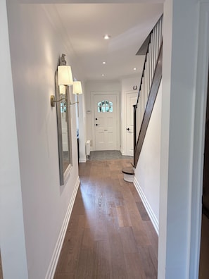 Ein Flur mit Holzboden, einer weißen Tür mit Fensterglas und einer Treppe mit schwarzer Handlauf.