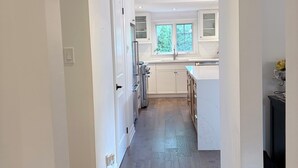 A narrow hallway leading to a kitchen with white cabinets, a window, and a door. - Premium South Leaside Retreat Steps to Bayview (Toronto)