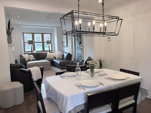 Ein Essbereich mit einem Tisch für vier Personen, einer modernen Chandelier und ein Wohnzimmer mit einer Couch und einem Kamin.