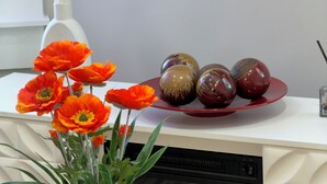 A modern kitchen with a white countertop, a white vase with green plants, and a red decorative plate with spherical objects.