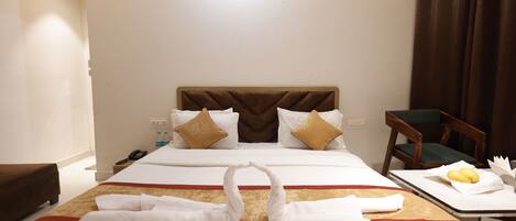 A hotel room with a neatly made bed, a bedside table with fruits, and a chair.