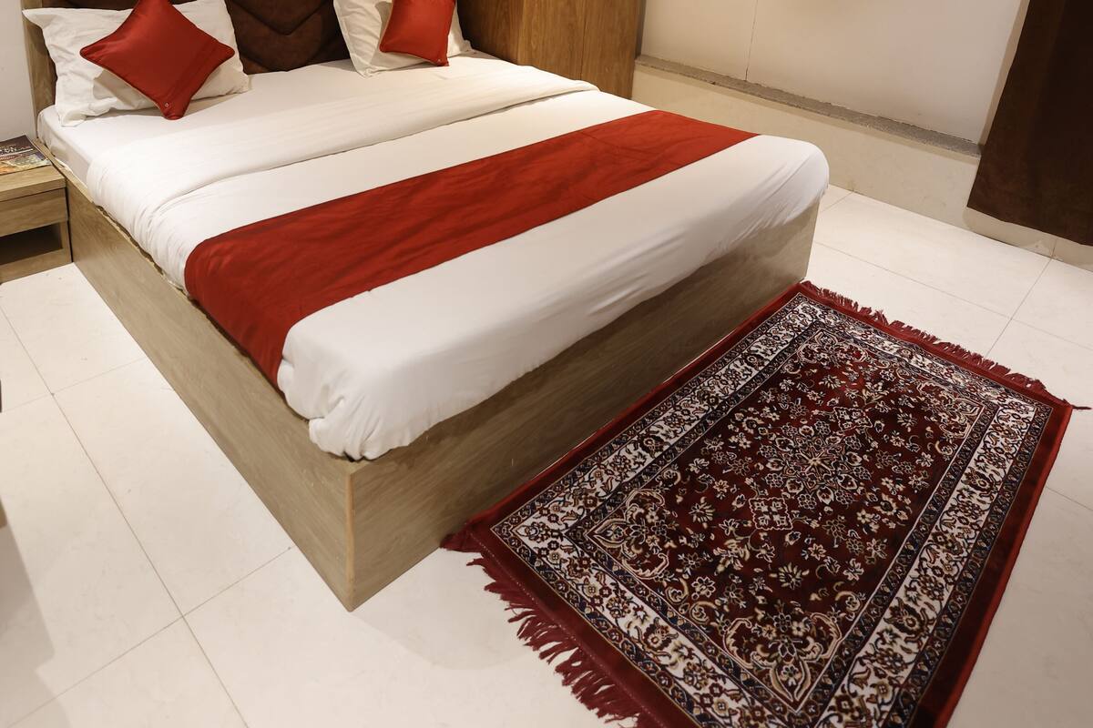 A bedroom with a bed, a wooden wardrobe, a ceiling fan, and a patterned rug.