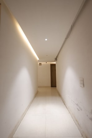 A narrow, well-lit hallway with white walls and a tiled floor, leading to a door at the end. - Hotel Royal Vilas (Bharatpur)