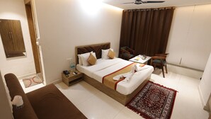 A hotel room with a bed, bedside table, chair, and a ceiling fan. - Hotel Royal Vilas (Bharatpur)