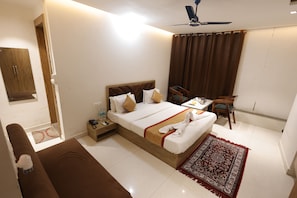 A hotel room with a bed, bedside table, chair, and a ceiling fan. - Hotel Royal Vilas (Bharatpur)