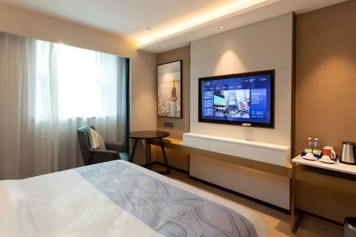 Ein Hotelzimmer mit einem Bett, einem an der Wand befestigten Fernseher, einem kleinen Tisch und einem Sessel.
