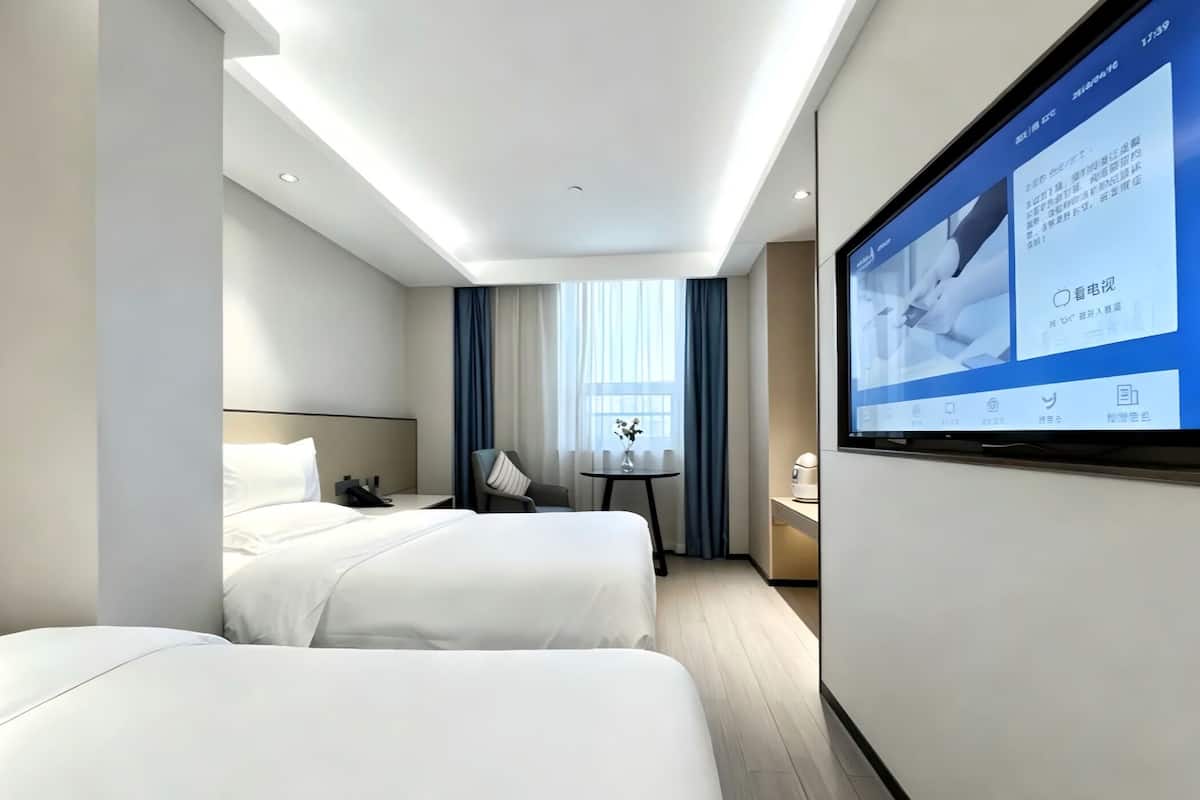 Ein modernes Hotelzimmer mit zwei Betten, einem Schreibtisch, einem Stuhl, einem Fernseher und einem Fenster mit Vorhängen.
