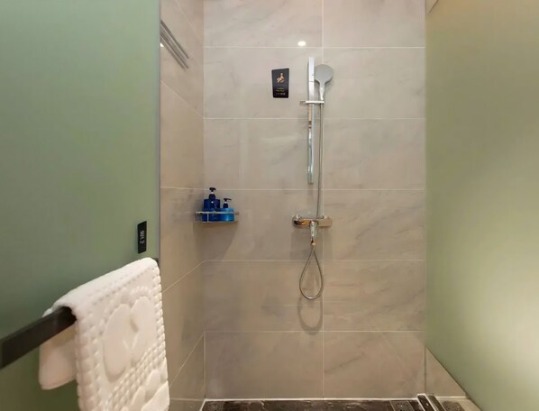 Ducha con cabezal de ducha de mano, grifo empotrado en la pared y un estante pequeño con artículos de aseo.