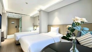 A hotel room with two beds, a desk, a chair, a vase with flowers, and a door leading to a bathroom. - Yeste International Hotel Wuhan Tiandi (Wuhan)