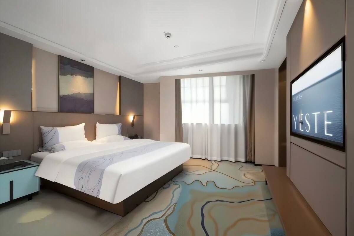 Ein Hotelzimmer mit einem großen Bett, einem Schreibtisch, einem Flachbildfernseher und einem an der Wand hängenden Kunstwerk.