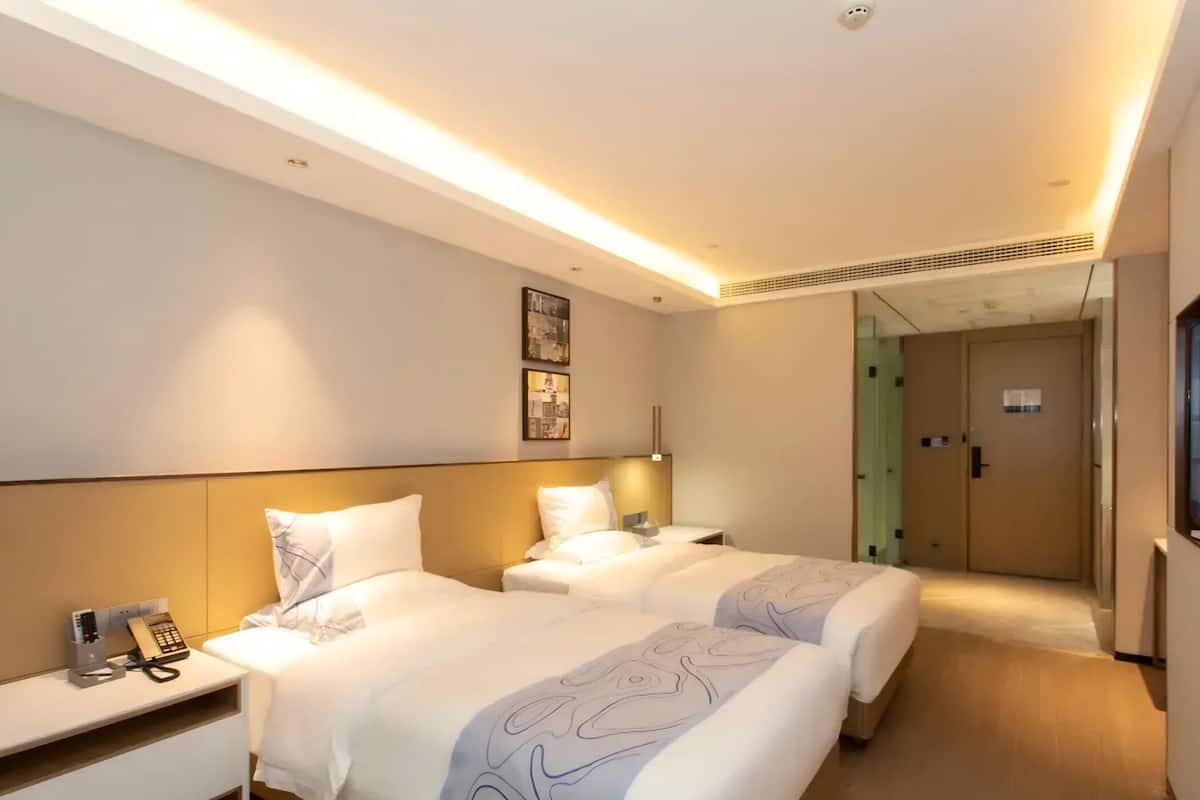 Ein Hotelzimmer mit zwei Betten, einem Nachttisch mit Telefon, einer Wandleuchte und einer Tür zu einem weiteren Raum.