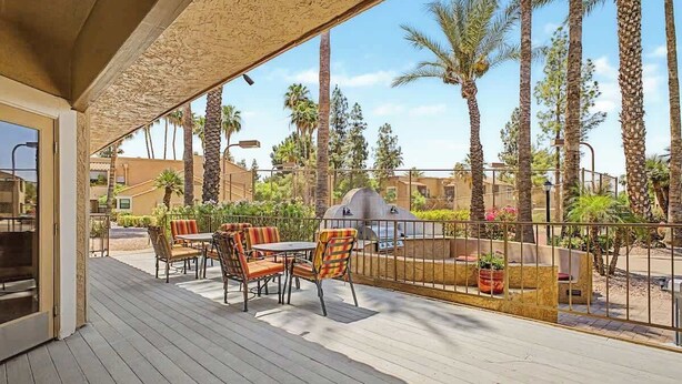 A covered outdoor patio with a table and chairs, surrounded by palm trees and a barbecue grill. - Central Scottsdale Haven Condo (Scottsdale)