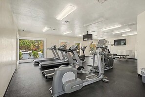 Ein Fitnessraum mit Laufbändern, Crosstrainern und einem Fernsehbildschirm.