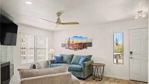 A living room with a sofa, a small table, a ceiling fan, a TV, and a window with blinds. - Central Scottsdale Haven Condo (Scottsdale)