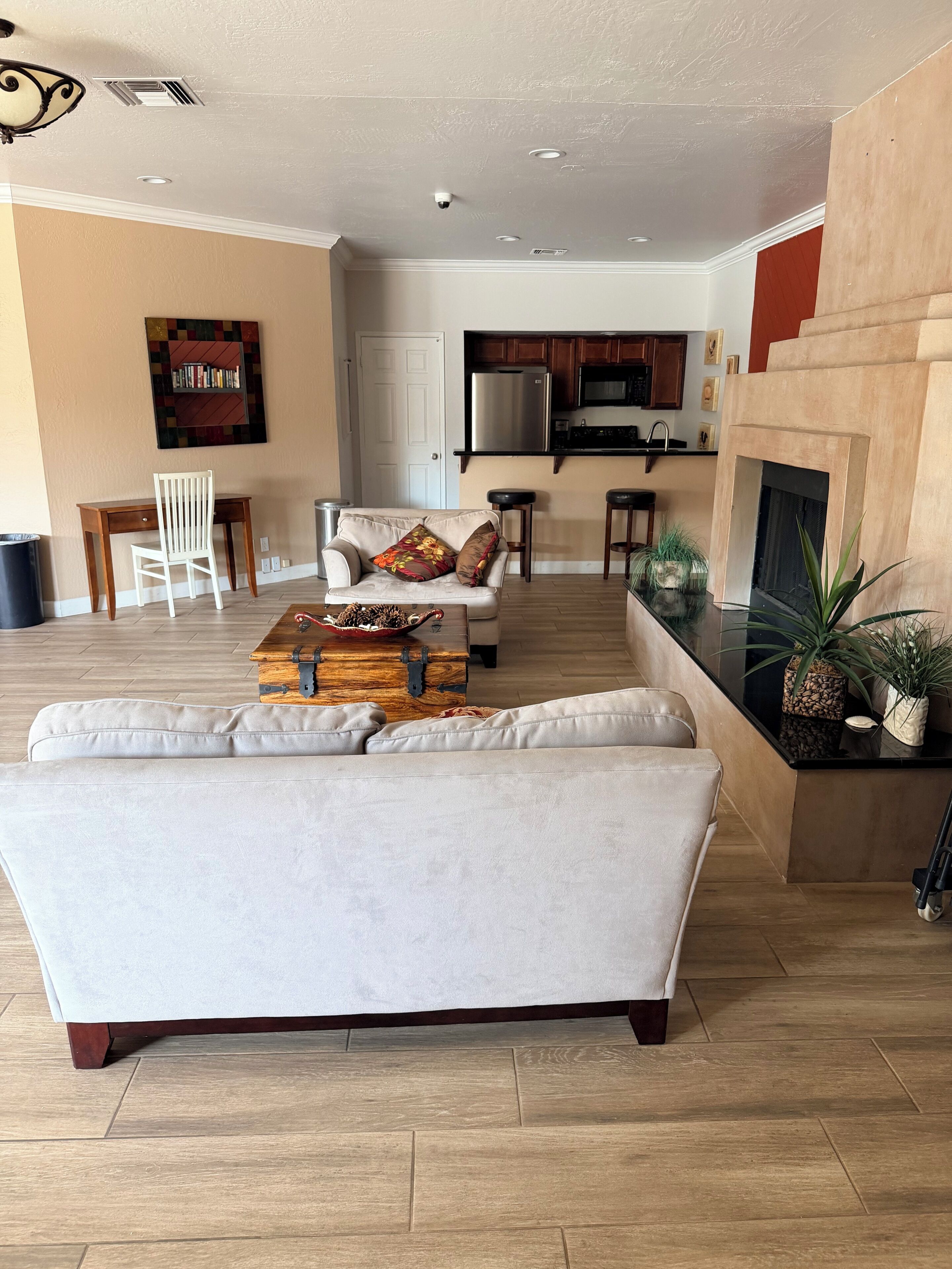 Un salon avec un canapé, une commode en bois, une table basse, une chaise blanche et, au fond, une cuisine.