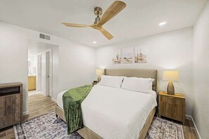 Ein Schlafzimmer mit einem Bett, einem Deckenventilator, einem Nachttisch mit Lampe und einem Wandbild.