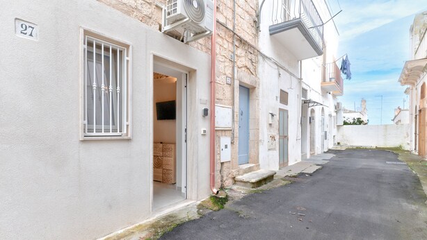 A narrow street with buildings, numbered 27, and a door with a basket inside. - Casetta Vé ,  Le Piccole Case Bianche (Ostuni)