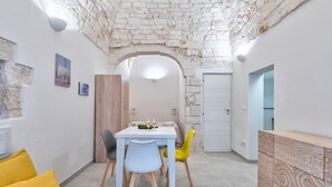 A dining area with a table, chairs, and a whiteboard. There is a stone wall and a door in the background. - Casetta Vé ,  Le Piccole Case Bianche (Ostuni)